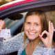 Young driver holding a license card and smiling from a car